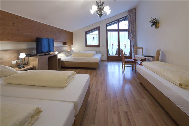 Ein geräumiges Zimmer mit zwei Einzelbetten und einem Doppelbett. Es gibt einen TV, einen Tisch und große Fenster, die viel Licht hereinlassen.