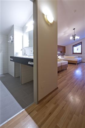 Ein modernes Zimmer mit zwei Betten und einem angrenzenden Badezimmer. Der Boden ist aus hellem Holz und das Licht ist freundlich.