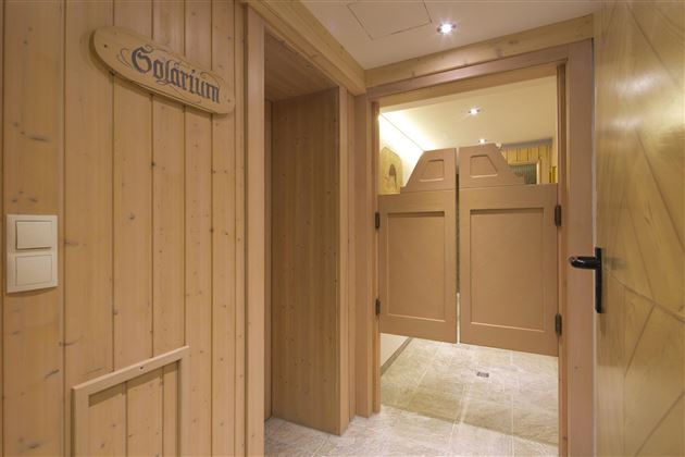 Ein gemütlicher Raum mit holzverkleideten Wänden und einem Schild mit der Aufschrift "Solarium". Der Eingang ist hell beleuchtet und führt zu einem weiteren Bereich.