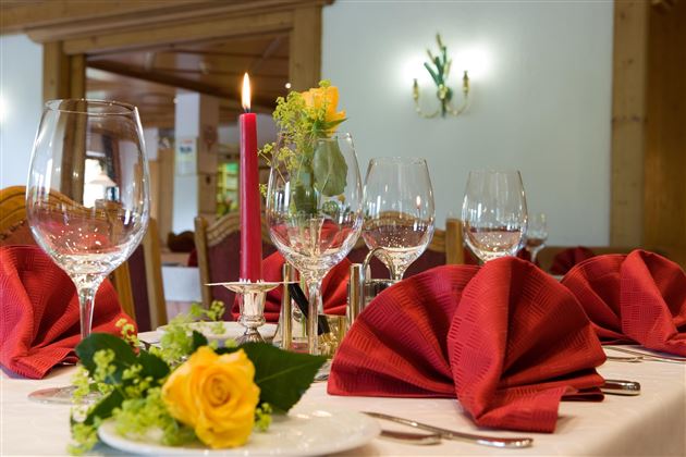 Ein elegant gedeckter Tisch mit roten Servietten und Weingläsern. Eine Rose und eine Kerze sorgen für eine romantische Atmosphäre.