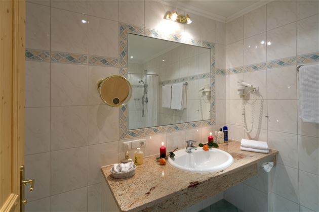 Ein modernes Badezimmer mit einem Waschbecken und einem großen Spiegel. Die Wände sind gefliest, und es gibt Handtücher sowie dekorative Kerzen.