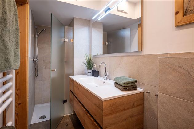 Een moderne badkamer met een douche en een houten wastafel. De wanddecoratie is in neutrale kleuren en er zijn verse planten als decoratie.