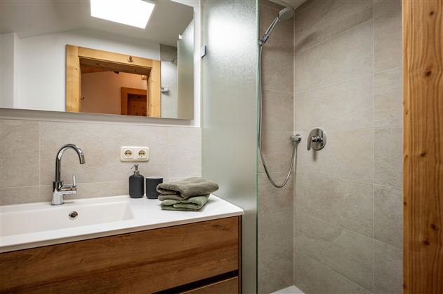 Een modern badkamer met een douche en een wastafel. De houten en tegel elementen geven de ruimte een hyggelige sfeer.