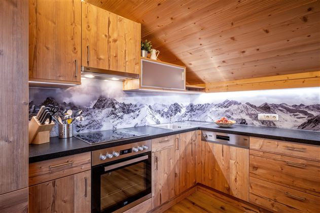 Een moderne keuken met houten kasten en een zwarte werkblad. Op de achtergrond is een indrukwekkend berglandschap afgebeeld.
