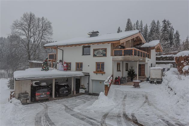 A beautiful house in the snow with a covered garage. The surroundings are wintry and peaceful.