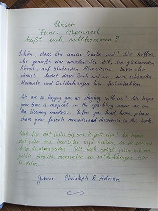 Een handgeschreven welkom in een notitieboek dat de gasten verwelkomt. Het bevat persoonlijke begroetingen van Yvonne, Christoph en Adnan.