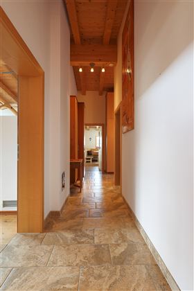 Ein heller Flur mit modernen Fliesen und Holzdetails. Auf der rechten Seite befinden sich Türen, die zu weiteren Räumen führen.