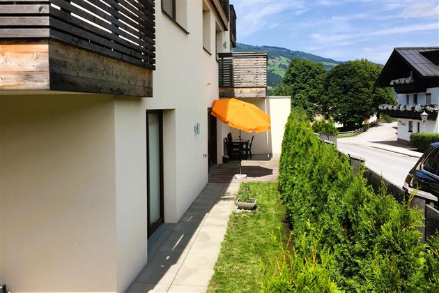Eine moderne Terrasse mit einem Sonnenschirm und Blick auf die Hecke. Im Hintergrund sind sanfte Hügel und Bäume zu sehen.