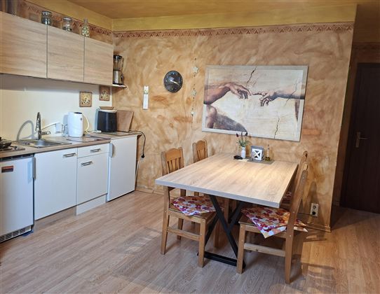 A modern kitchen with wooden cabinets and a wooden dining table. On the wall hangs a picture that shows an artistic representation of two hands.