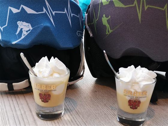 Zwei Gläser mit Dessert und Sahne stehen auf einem Tisch. Im Hintergrund sind Skihelme mit verschiedenen Designs zu sehen.