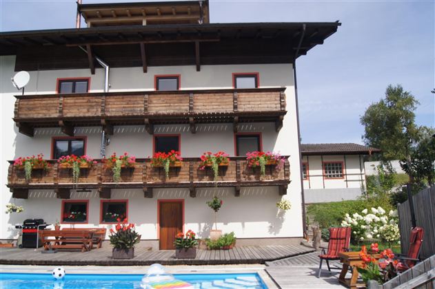Ein hübsches Haus mit Balkonen und blühenden Pflanzen. Der Swimmingpool im Vordergrund lädt zum Entspannen ein.