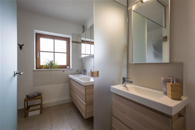 Ein modernes Badezimmer mit Holzschränken und einem großen Spiegel. Es gibt auch ein Fenster, das natürliches Licht hereinlässt.