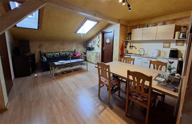 A bright attic apartment with a living room and a small kitchenette. The dining area is equipped with a wooden table and chairs.