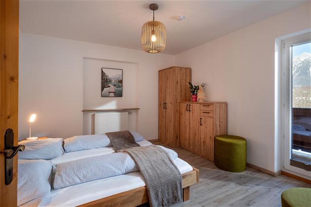 Een gezellige slaapkamer met een houten bed en een moderne lamp. De ruimte is licht en minimalistischer ingericht, met een grote raamkozijnen en een mooi uitzicht naar buiten.