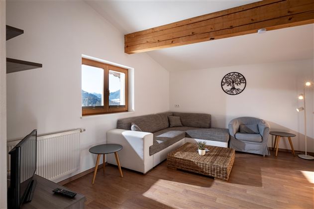 Een lichte woonkamer met een gezellige bank en een fauteuil. Grote ramen bieden uitzicht op de bergen en zorgen voor veel daglicht.