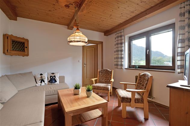 Ein gemütliches Wohnzimmer mit einem hellen Sofa und zwei Holzstühlen. Große Fenster bieten einen Blick auf die Landschaft.