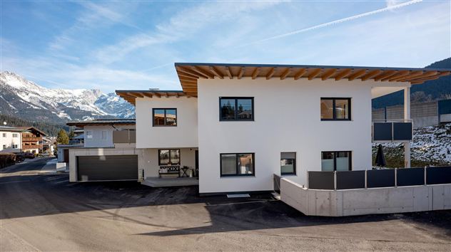 A modern building with a white facade and wood details. Snow-covered mountains are visible in the background.