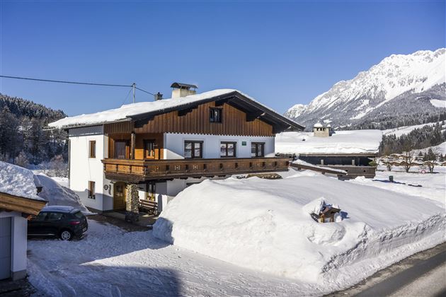 A charming house in the snow with a balcony and a beautiful mountain landscape in the background. The surroundings are wintry and peaceful.