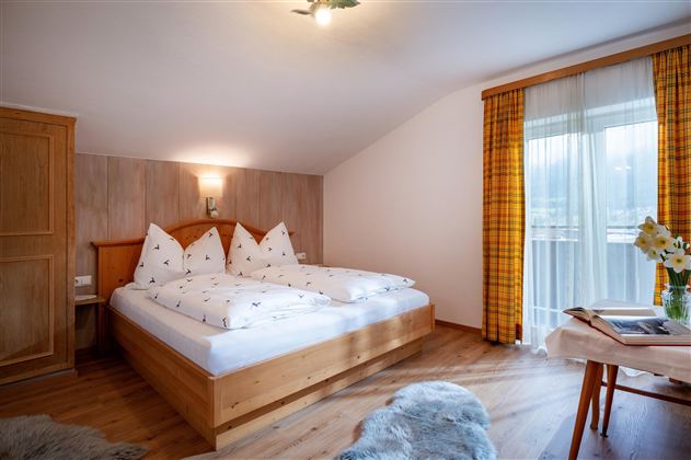 A cozy bedroom with a double bed and decorative pillows. Large windows provide plenty of daylight and a view outside.