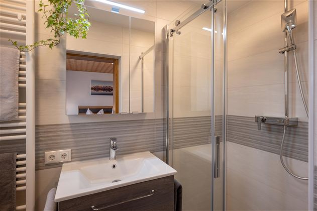 A modern bathroom with a glass cubicle and a sleek sink. The walls are bright, and a plant adds a touch of green.