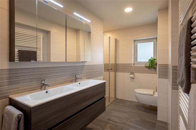 A modern bathroom with two sinks and large mirrors. It features bright tiles and a shower with glass partition.