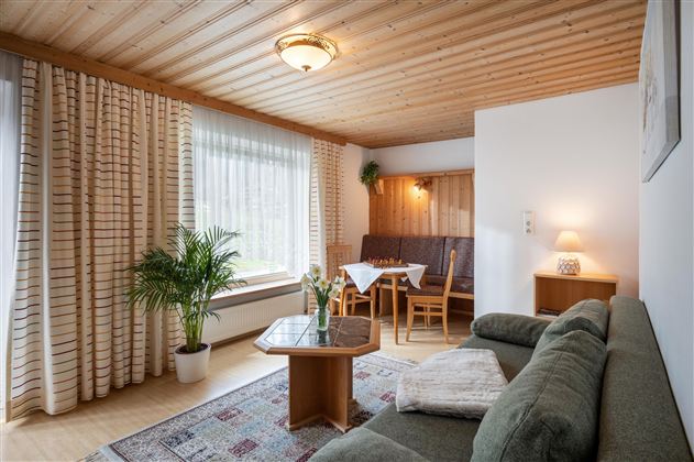 A cozy living room with a sofa, a table, and chairs. Large windows let in plenty of light and give the room an inviting atmosphere.
