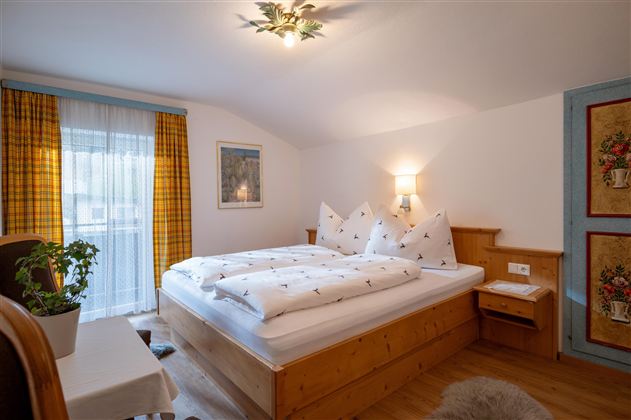 A cozy bedroom with a double bed and wooden furniture. Large windows let in plenty of light and create an inviting atmosphere.