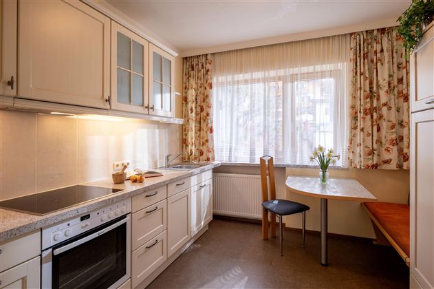 A bright kitchen with modern furniture and a large window. The table is decorated with fresh flowers and there are placed chairs.
