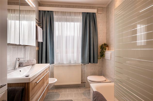 A modern bathroom with wooden details and white walls. Curtains in blue and a bright, inviting atmosphere.