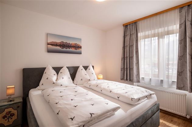 A cozy bedroom with two single beds and light curtains. A landscape picture hangs on the wall, emphasizing the relaxing atmosphere.