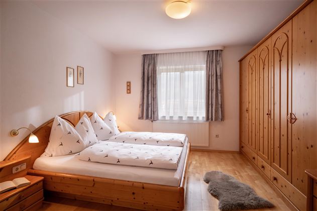 A cozy bedroom with two single beds and wooden furniture. The room is bright and friendly, with a window that lets in plenty of light.