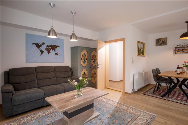 A modern living room with a comfortable sofa, a table, and a dining group. A world map hangs on the wall and the room is bright and inviting.