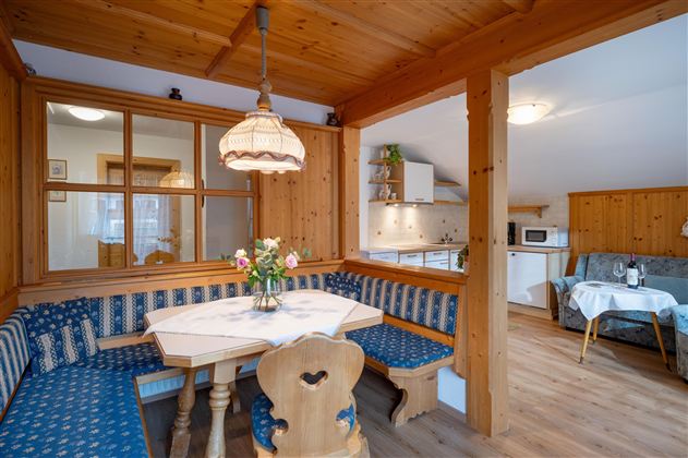 A cozy kitchen with a wooden style and a dining table. The decor is bright and friendly, with blue fabric covers and a beautiful bouquet of flowers on the table.