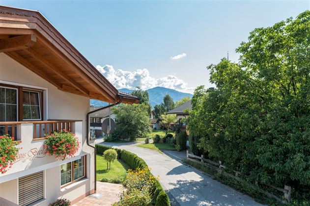 A charming landscape with a modern house and a beautiful garden. In the background, mountains and a clear blue sky can be seen.