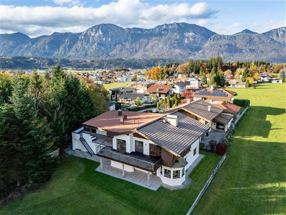 Eine attraktive Wohngegend mit modernen Häusern und einem großen Garten. Im Hintergrund erstrecken sich beeindruckende Berge und ein klarer Himmel.