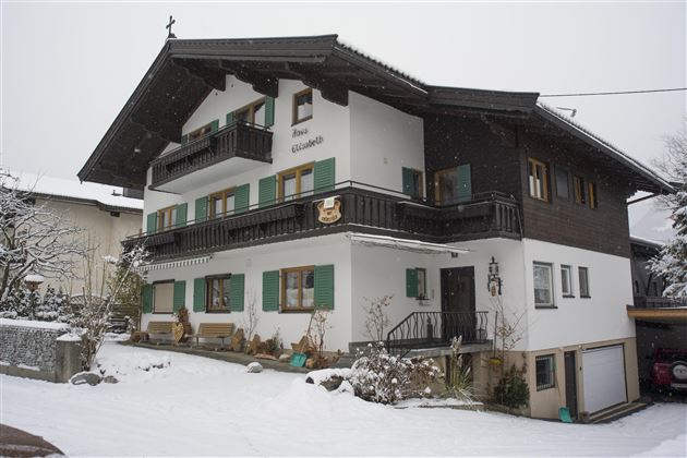 Ein charmantes Haus im alpinen Stil, umgeben von Schnee. Die Fensterläden sind in einem grünen Farbton gehalten und verleihen dem Gebäude eine gemütliche Atmosphäre.