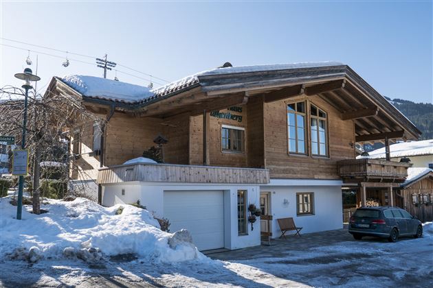 A traditional wooden cottage in the snow. The surrounding area is wintry with a clear blue sky.