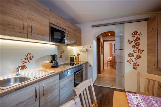 Eine moderne Küche mit Holzschränken und einem eleganten Design. Im Hintergrund ist ein gemütlicher Essbereich zu sehen.