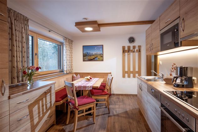 Eine moderne Küche mit Holzschränken und einer gemütlichen Sitzecke. Am Tisch stehen frische Blumen und eine schöne Aussicht durch das Fenster.