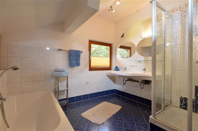 A modern bathroom with a bathtub and a shower cabin. The room has light walls and a large window opening.
