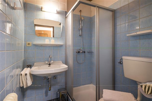 A small bathroom with blue tiles. It contains a shower cabin, a sink, and a toilet.