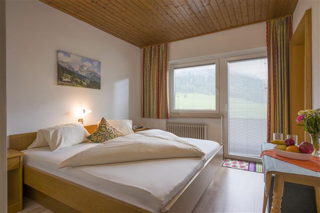 A cozy bedroom with a double bed and bright walls. Large windows provide a view of the surrounding landscape.