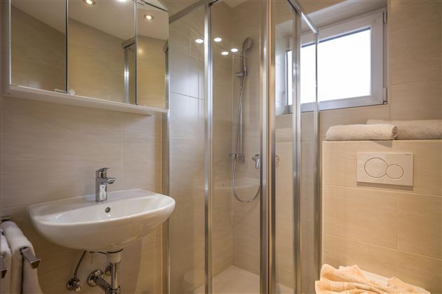 A modern bathroom with a shower cabin and a sink. Bright tiles and a window create a friendly atmosphere.