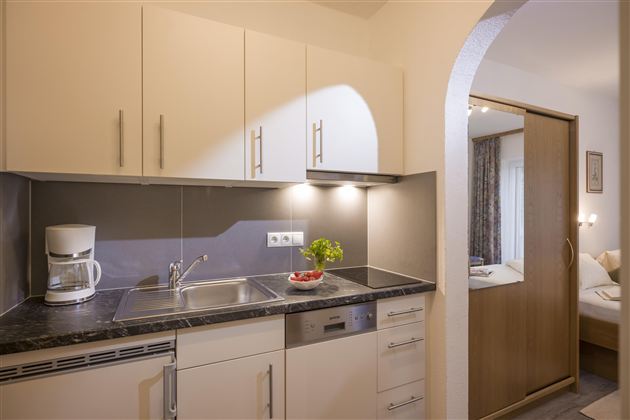 A modern kitchen with bright cabinets and a countertop. In the background, a cozy bedroom is visible.