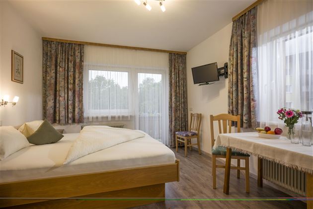 A cozy bedroom with a double bed and a table. Bright curtains and a pleasant atmosphere make the room inviting.
