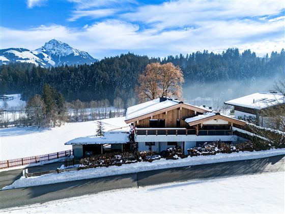 Een mooi winterhuis omgeven door met sneeuw bedekte velden en bergen. De lucht is helder en de sneeuw glinstert in de zon.