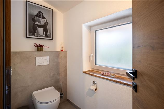 A modern bathroom with a toilet and a window. On the wall hangs a poster-like picture of a person on the toilet.