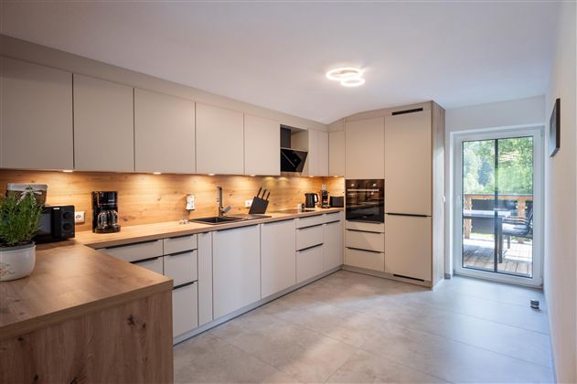 Modern kitchen with bright cabinets and wooden details. Large windows provide plenty of light and a view outside.