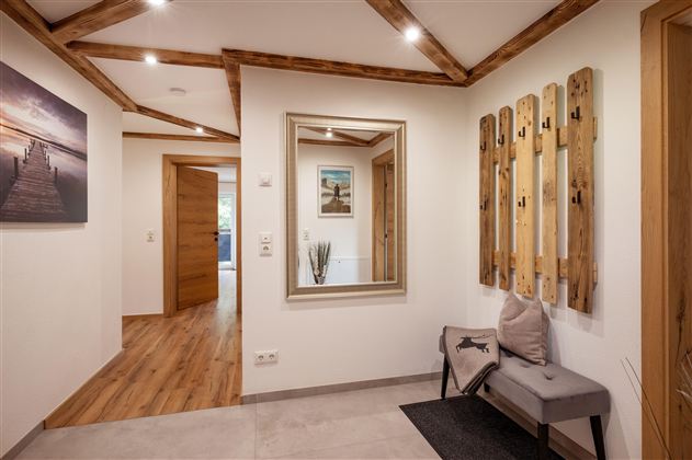 A modern hallway with wooden details and a large mirror. Wooden strips hang on the wall, and a side chair provides additional comfort.