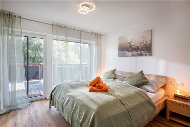 A cozy bedroom with a large bed and soft green colors.  
Large windows let in plenty of daylight and create a pleasant atmosphere.